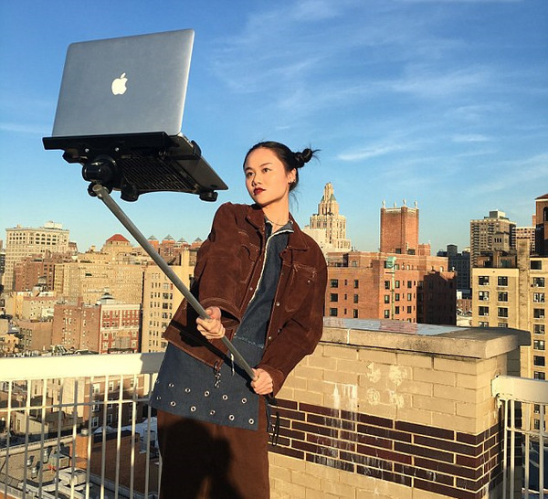 一位年轻人举着Macbook笔记本电脑自拍（网页截图）