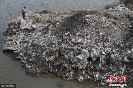 资料图：2016年7月17日，江苏省海门市的江心沙农场新江海河一座桥附近偷倒的垃圾。据运载垃圾货船上的船员透露，这些垃圾也是从上海运来。视觉中国
